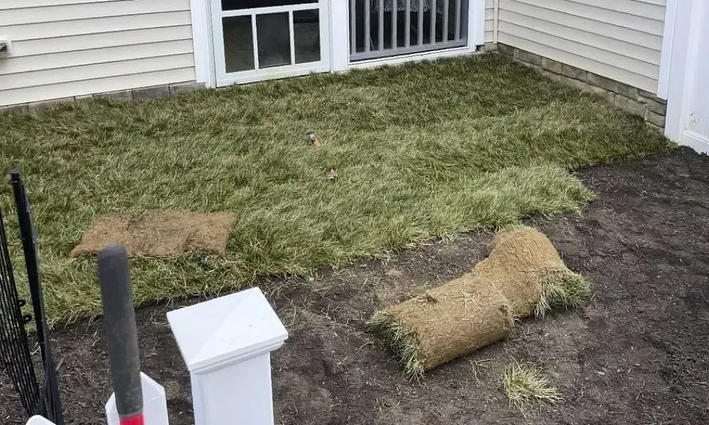 A lawn outside a house is in the process of being covered with the sod installation to depict the