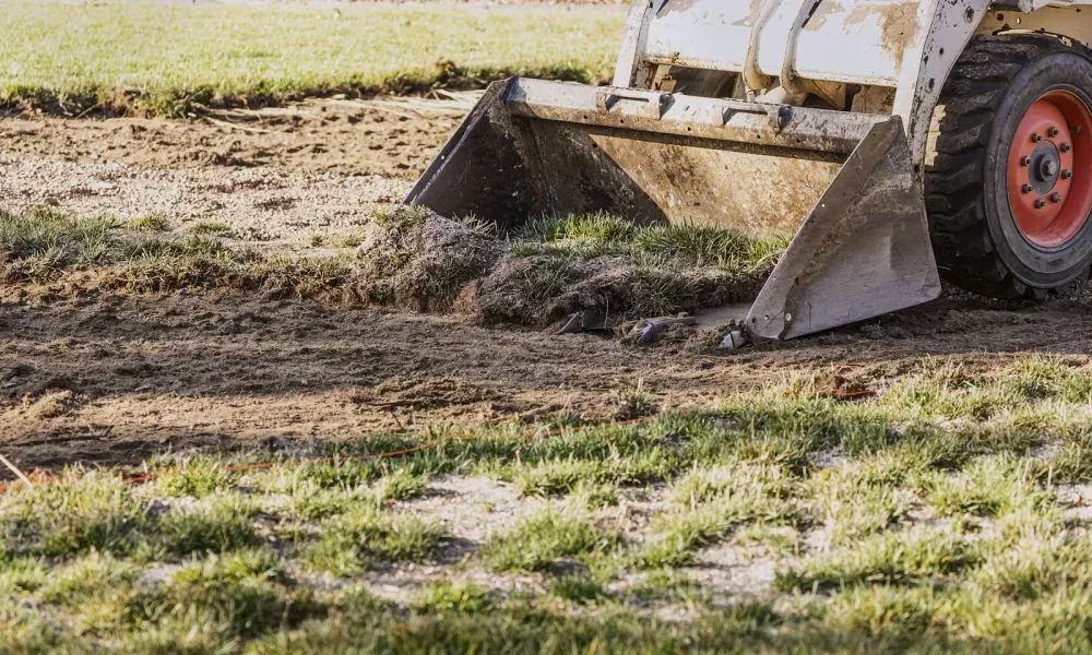A small bulldozer removing ground level grass and mud to level the yard for improved landscape