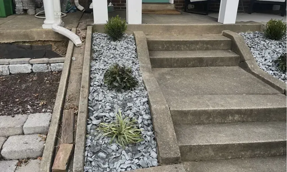 A small slide alongside house stairs covered with various gray pebbles and few bunch of plants