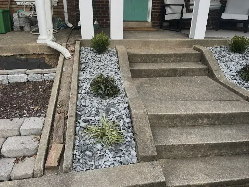 A small slide alongside house stairs covered with various gray pebbles and few bunch of plants making a good outdoor design