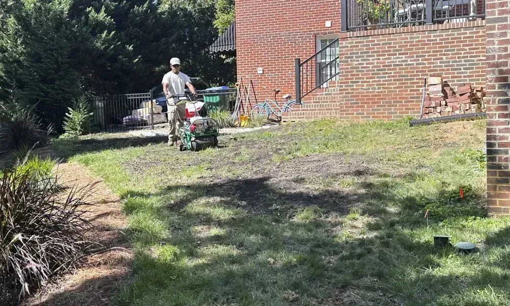 A wide angle shot of a person doing professional lawn aeration around a house in daylight