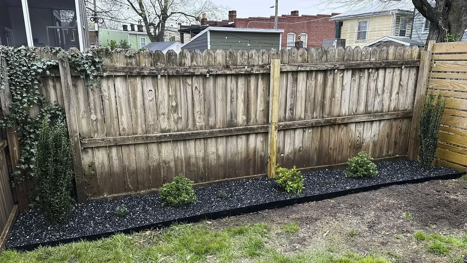 Lawn enclosed by wooden boundary wall with a section of pebbles interspersed with plants showcasing unique garden design