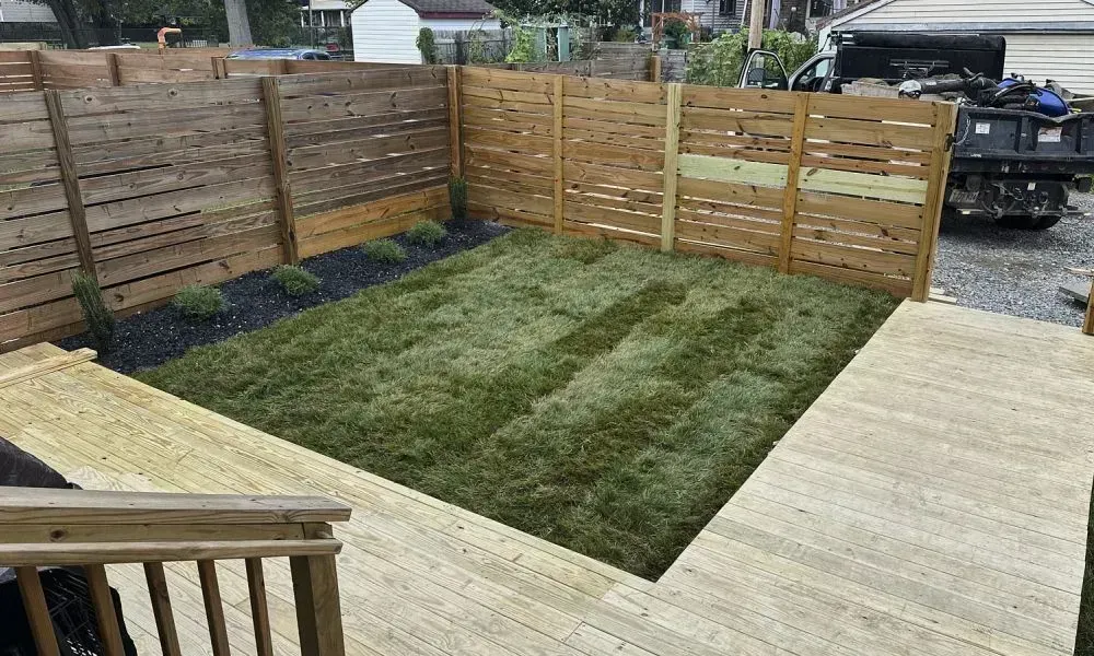 Lawn enclosed by wooden boundary wall with ground level grass and a newly constructed wooden
