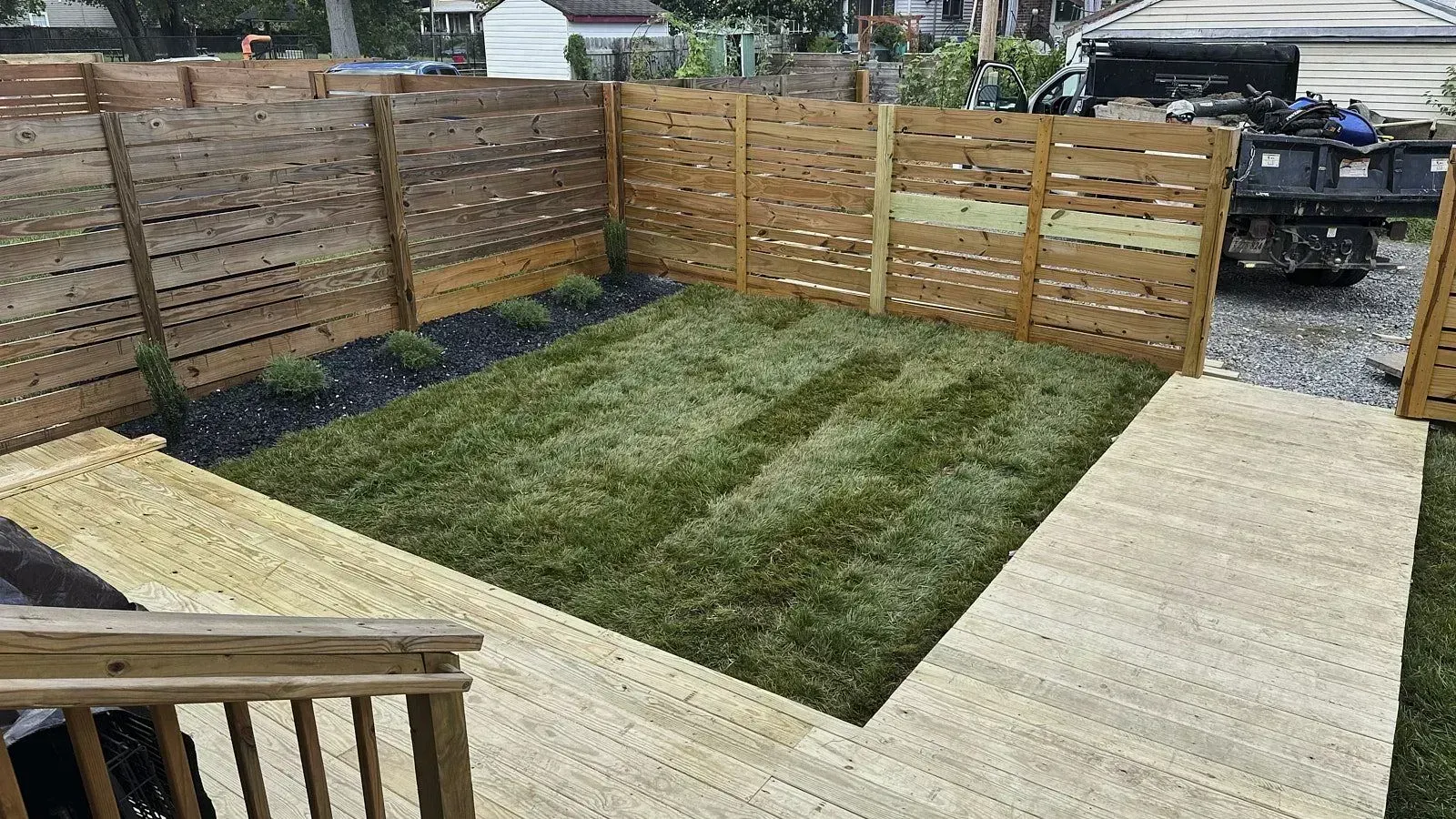 Lawn enclosed by wooden boundary wall with ground level grass and a newly constructed wooden pathway for better yard design