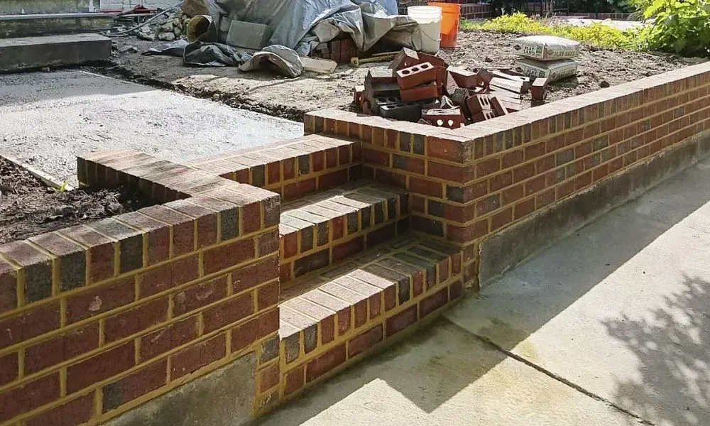 Red brick boundary under construction around a lawn where the bricks are filled with yellow cement