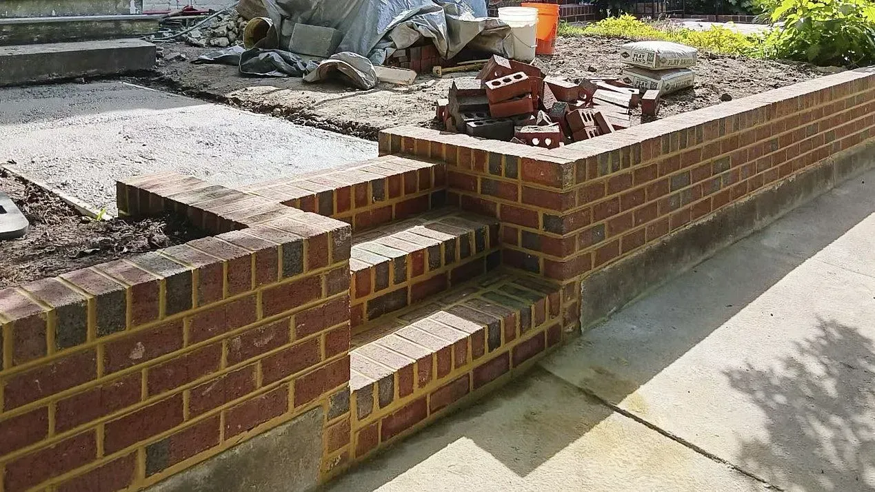 Red brick boundary under construction around a lawn where the bricks are filled with yellow cement for enhanced garden design
