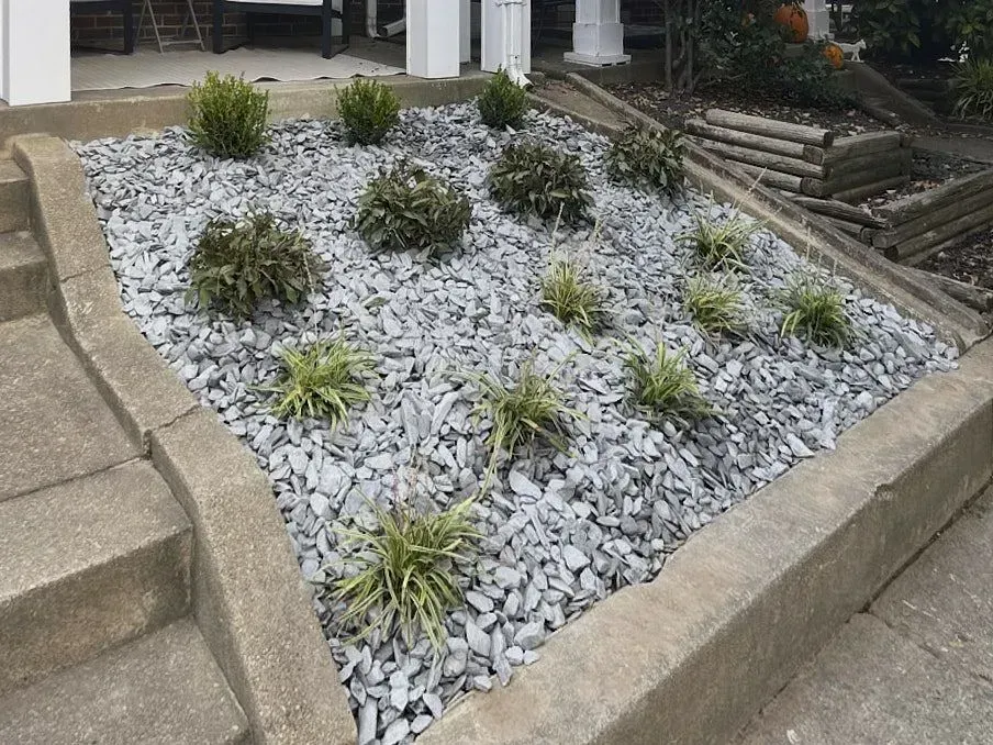 Wide slidedown alongside house stairs covered with gray pebbles and have various plants creating a unique outdoor design